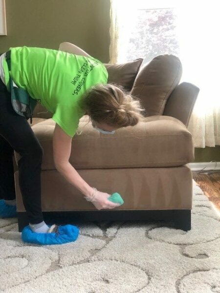 A woman cleaning a couch in a living room.