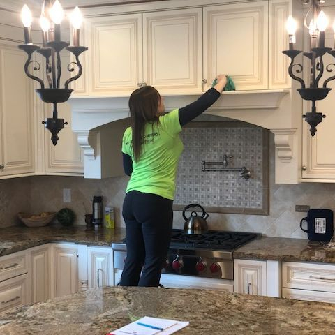 A woman cleaning a kitchen in a green shirt.